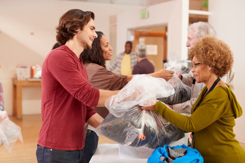 People Donating Clothing To Charity Collection In Community Center